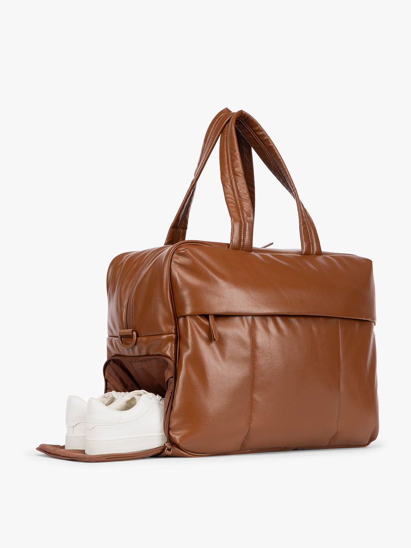 Side shoe compartment of Honey Brown CALPAK Luka Large Duffel in vegan leather with dual top handles, shown against a plain white background