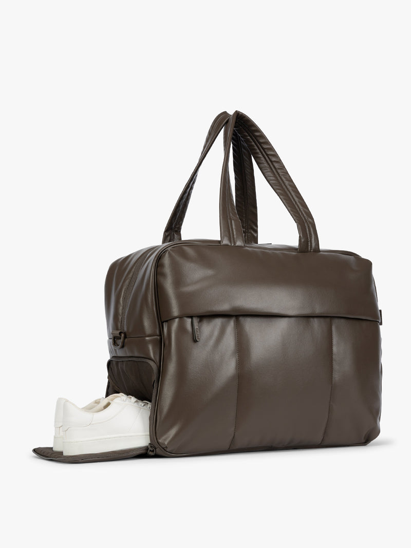 Side shoe compartment of Mushroom dark brown CALPAK Luka Large Duffel in vegan leather with dual top handles, shown against a plain white background