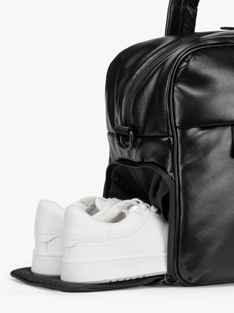 Side shoe compartment of the Black CALPAK Luka Duffel in vegan leather with dual top handles and a front zippered pocket, photographed against a clean white background