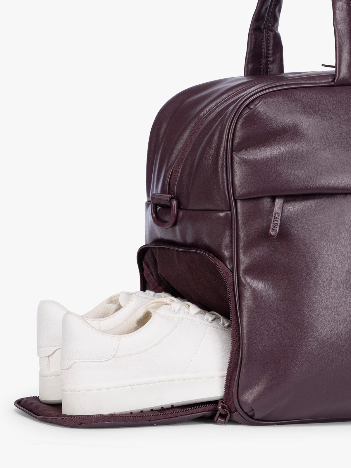 Side shoe compartment of a dark burgundy CALPAK Luka Duffel in vegan leather with dual top handles and a front zippered pocket, photographed against a clean white background; DSM1901-DARK-CHERRY-PU