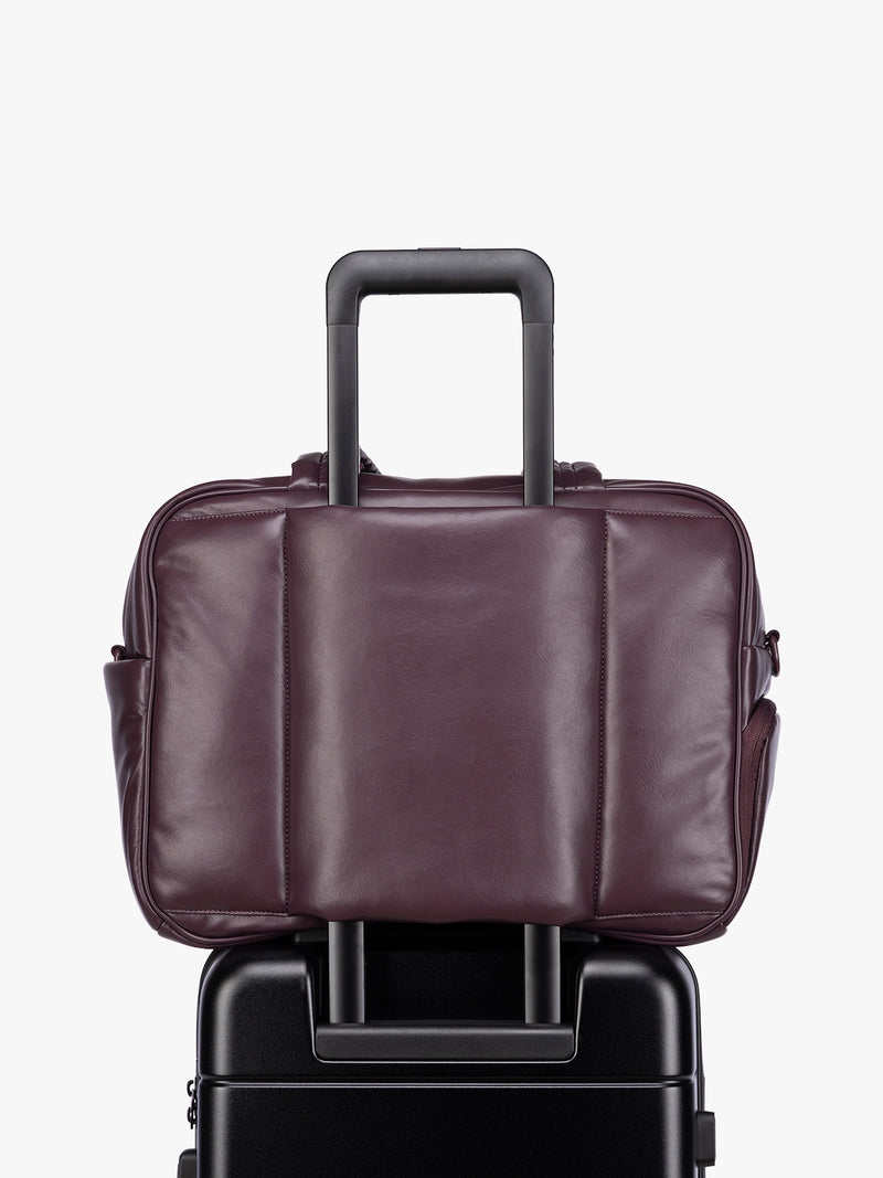Luggage trolley sleeve of a dark burgundy CALPAK Luka Duffel in vegan leather with dual top handles and a front zippered pocket, photographed against a clean white background