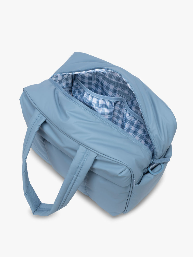 Opened view of CALPAK Luka Duffel in light blue French Blue with interior white and blue gingham print