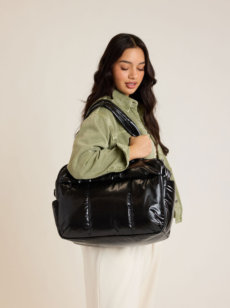 Model weraing CALPAK Luka Duffel in shiny black on a white background