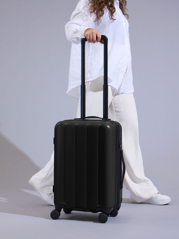 Model rolling CALPAK Evry Carry-On Luggage by dual spinner wheels in black