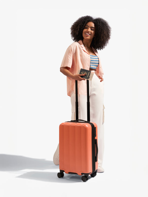 Model holding handle of CALPAK Evry Carry-On Luggage in orange persimmon