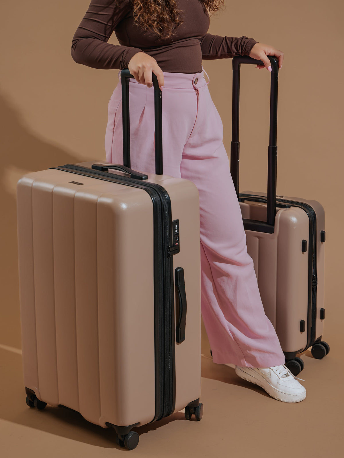 Model standing besides CALPAK Evry Large Luggage and CALPAK Carry-On Luggage in brown; LCO1028-CHOCOLATE