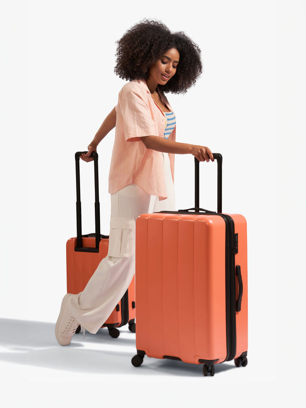 Model rolling CALPAK Evry Carry-On Luggage and Evry Large Luggage in persimmon