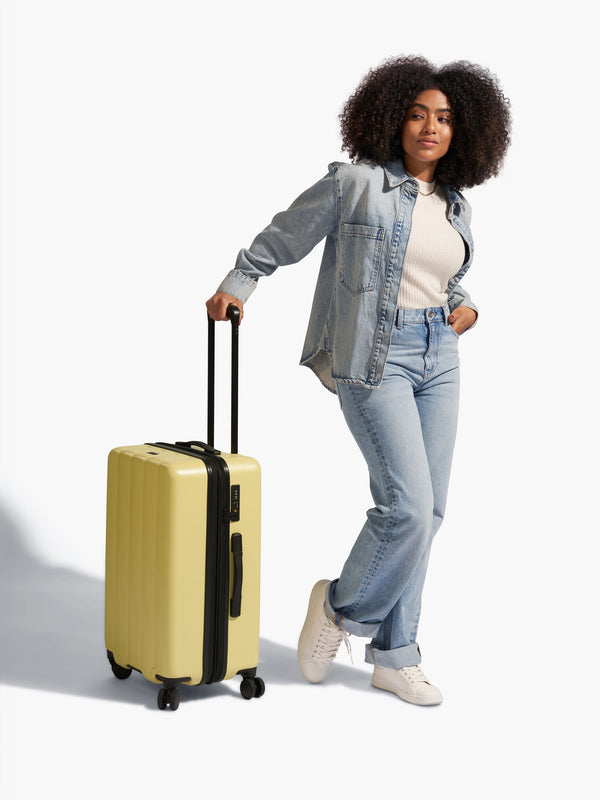 Model standing besides CALPAK Evry Medium Carry-On Luggage in yellow butter