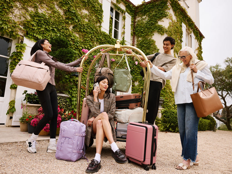 Family of grandma, mom, son and daughter in front of a hotel with a luggage trolley filled with CALPAK bags and luggage
