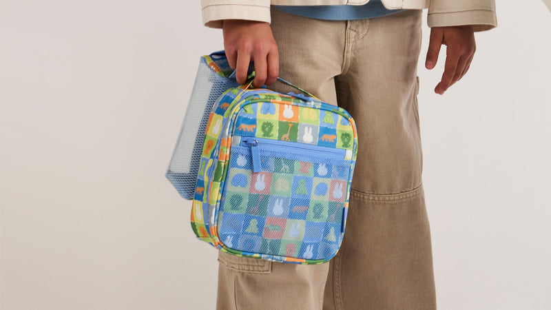 Child holding the CALPAK + Miffy Everything Cube in Blue Zoo Trip featuring blues, yellow, and green tiles with Miffy and animal characters