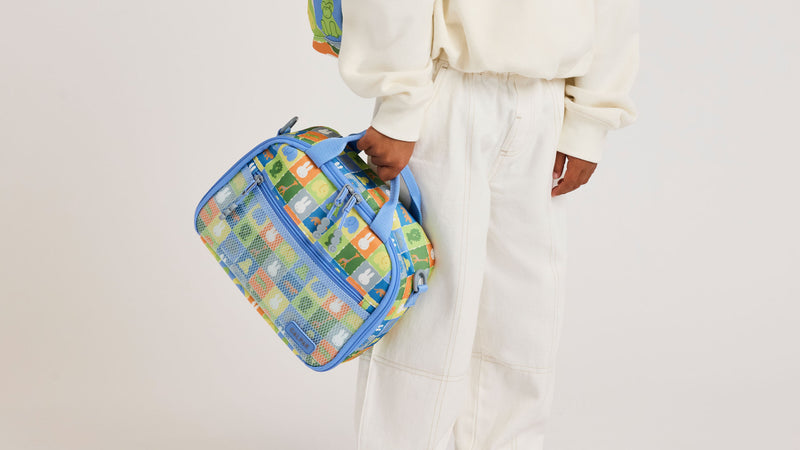 Boy holding the Colorful CALPAK Kids Lunch Bag with Miffy and other animal characters, with durable handles