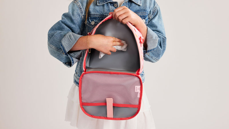 Child's hand wiping the CALPAK Kids Lunch Bag that is pink and colorful