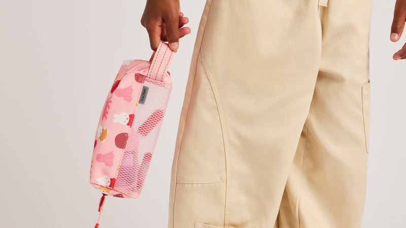 Child holding the side grab handle of the CALPAK kids pencil case in Miffy pink zoo trip 
