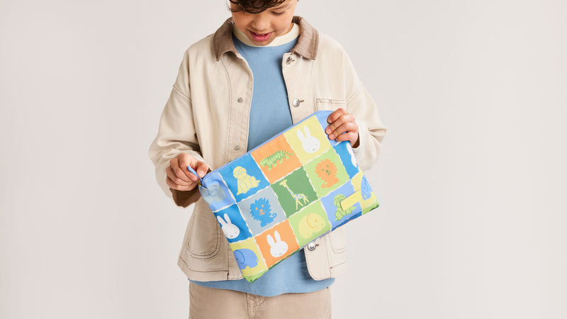 Child opening the CALPAK + Miffy Packing Cube Set in Miffy Blue Trip featuring Miffy and other animal characters with a zippered top 