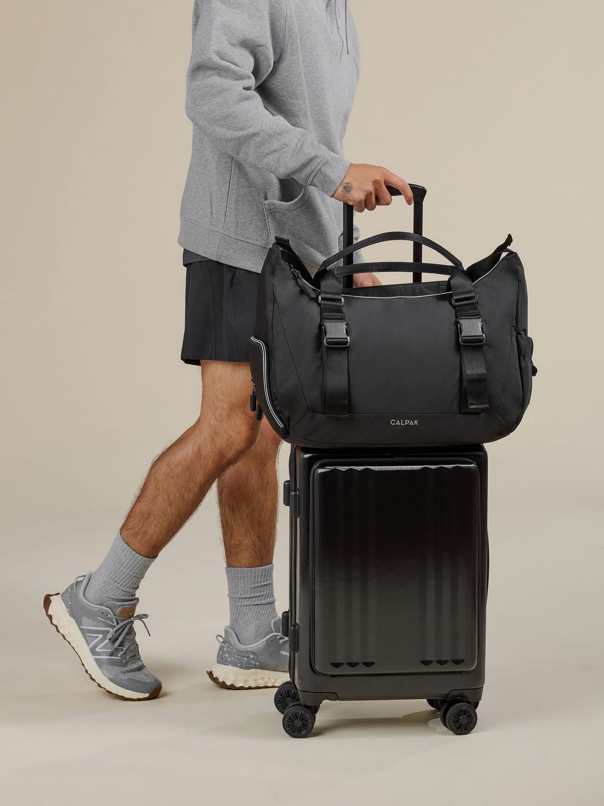 Model rolling CALPAK Ambeur Front Pocket Carry-On Luggage with CALPAK Fit Gym Bag secured by luggage trolley sleeve in black; TBF2401-BLACK, BTBF2401-BLACK