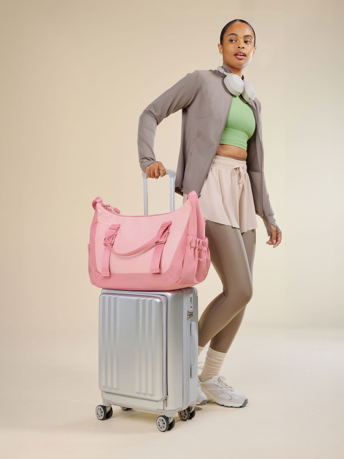 Model rolling CALPAK Ambeur Front Pocket Carry-On Luggage with tea rose pink CALPAK Fit Gym Bag secured by luggage trolley sleeve; TBF2401-TEA-ROSE, BTBF2401-TEA-ROSE