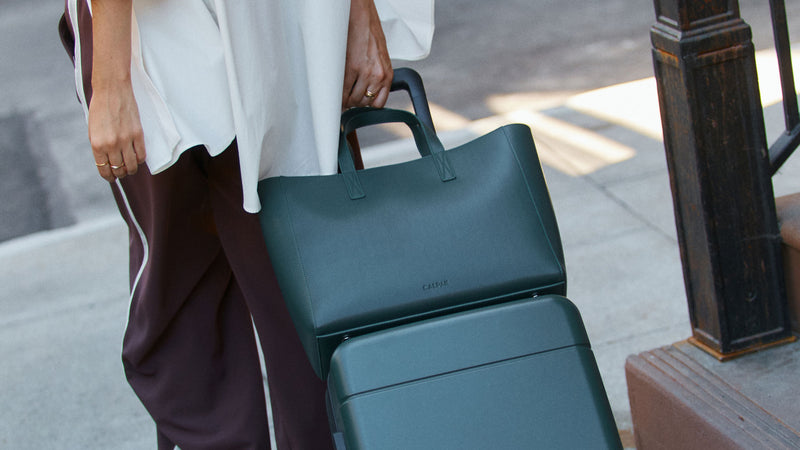 Person holding dark green Forest Haven Tote on a luggage with trolley sleeve