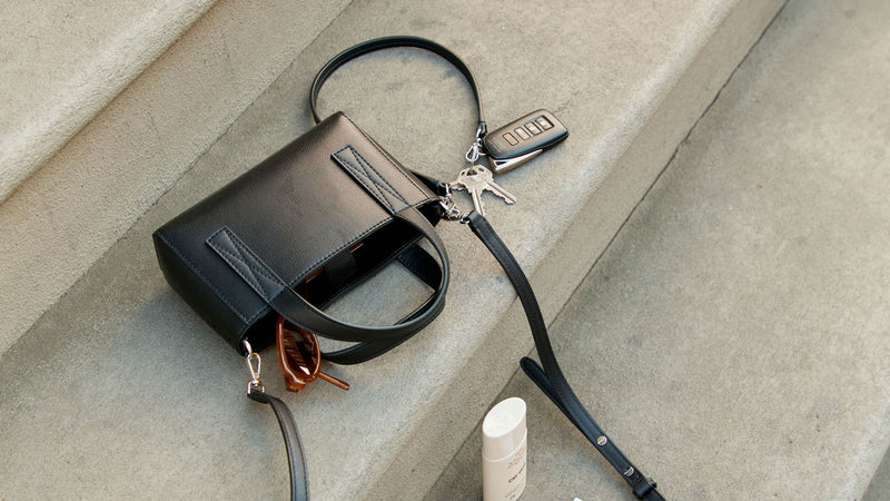 CALPAK Haven Mini Crossbody Tote in black with keys and a lip balm on a concrete surface