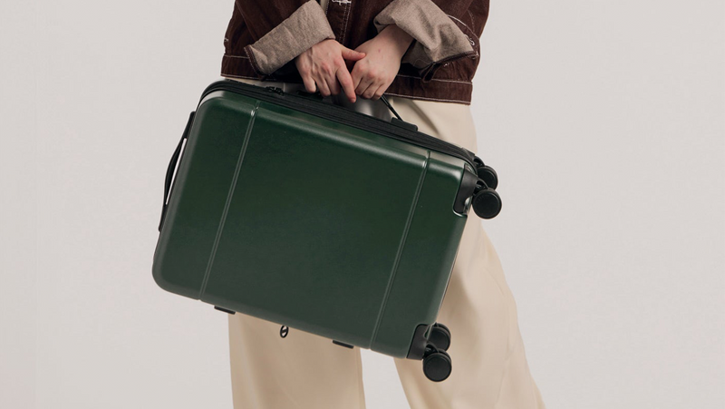 Model holding the Hue Carry On Luggage in green Emerald by the side handle