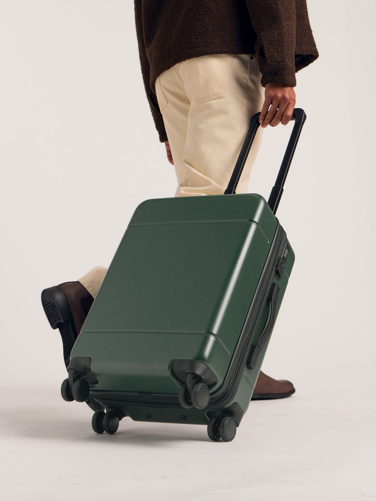Model rolling CALPAK Hue Carry-On Luggage hard shell in green emerald; LHU1020-NP-EMERALD