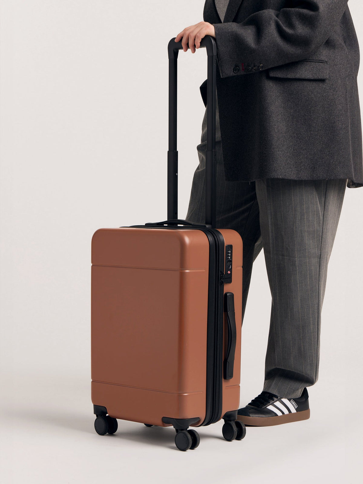 Model with CALPAK Hue hard shell rolling carry-on luggage in pink sand color; LHU1020-NP-HAZEL