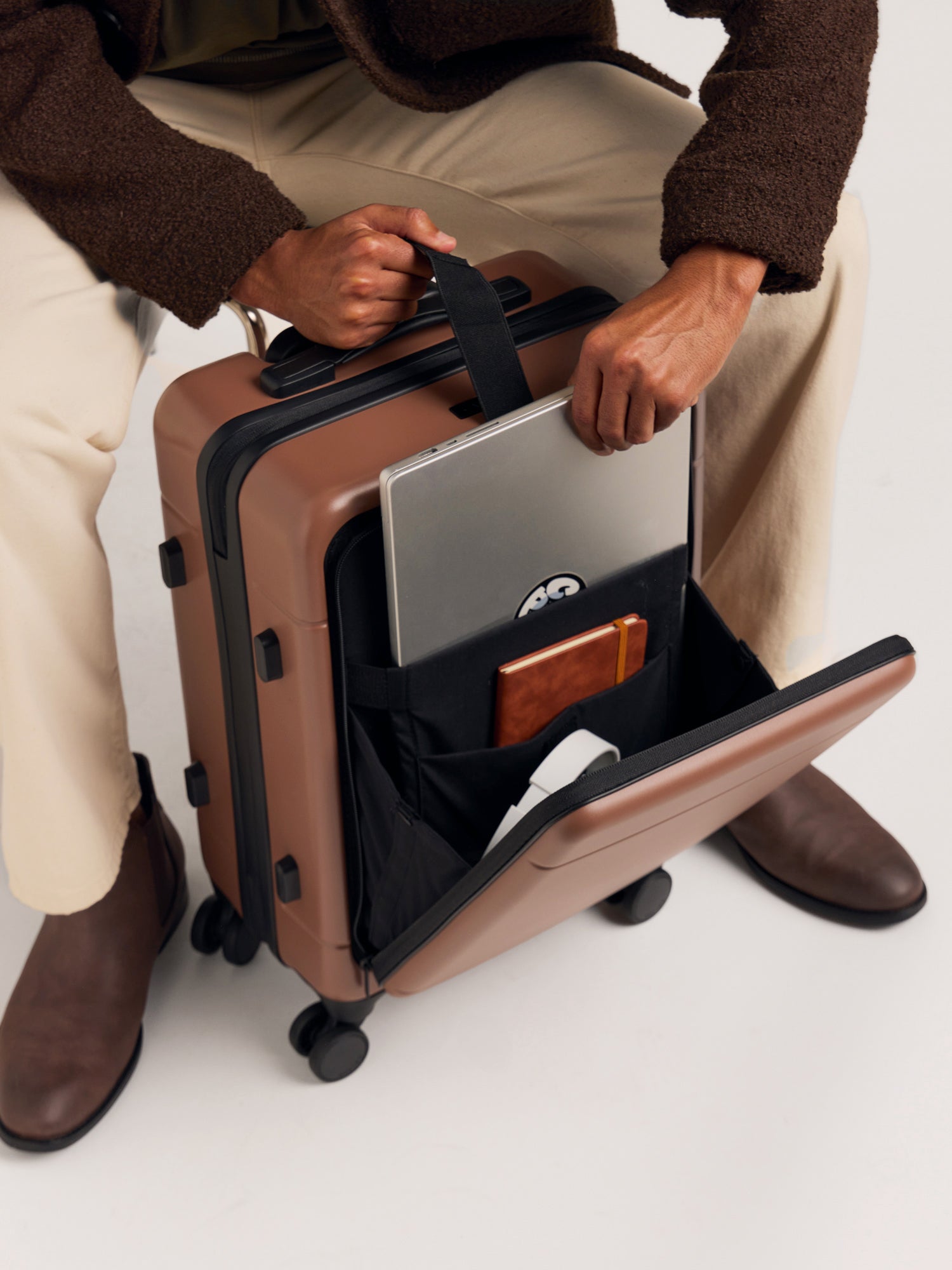 Front-laptop compartment with model putting in laptop in the CALPAK Hue Front Pocket Carry-On Luggage in Hazel; LHU1020-HAZEL