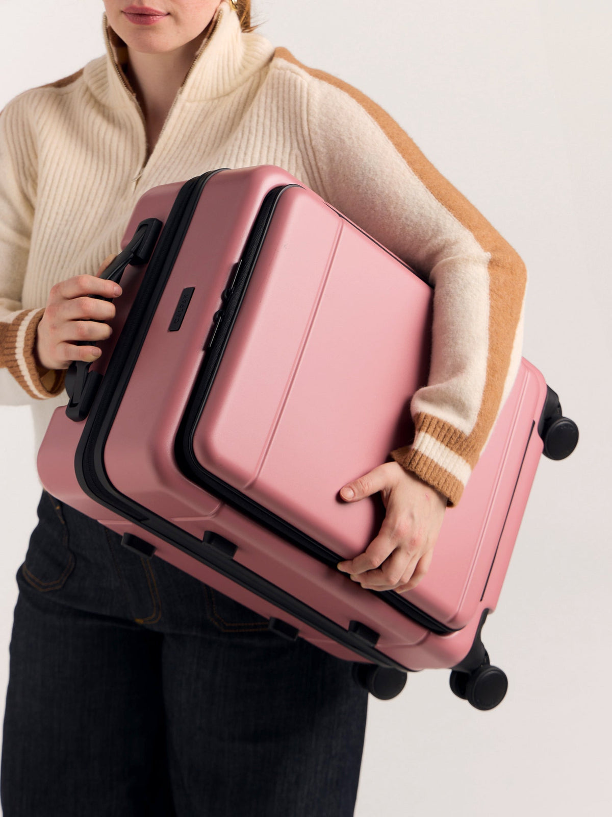 Model holding CALPAK Hue Front Pocket Carry-On Luggage with hard shell carry-on spinner luggage with front-laptop compartment in Mauve under the arm; LHU1020-MAUVE