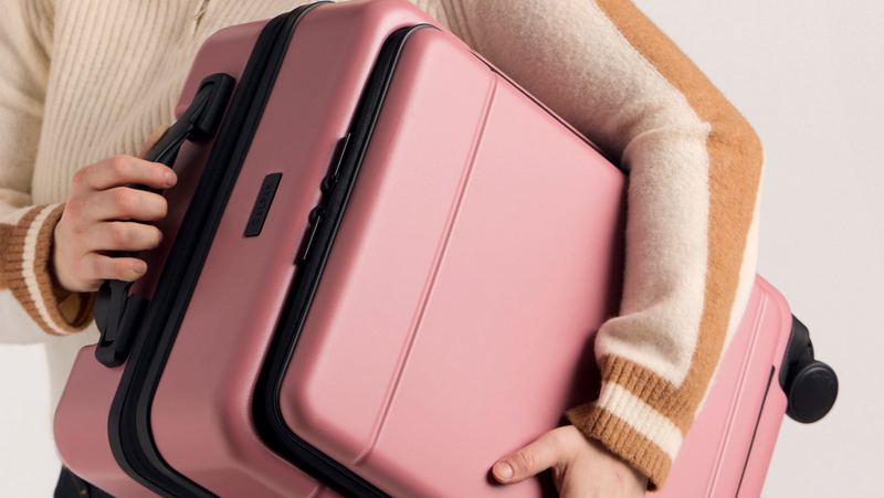 Woman carrying the CALPAK Hue Front Carry On Luggage in pink Mauve