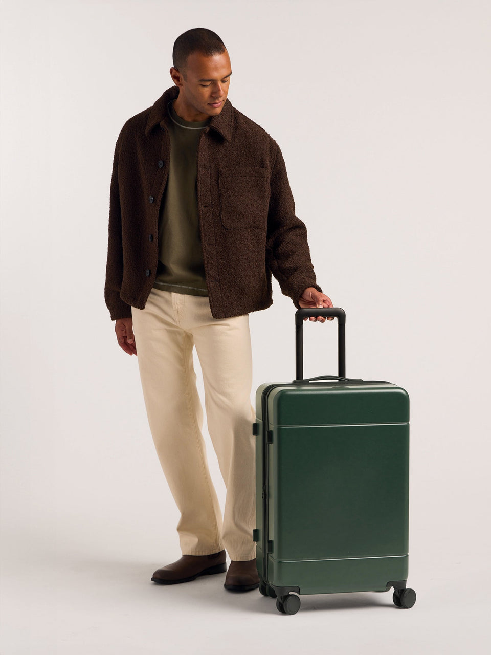 Model holding handle of the CALPAK Hue Medium & Large Luggage in green Emerald; LHU1024-EMERALD