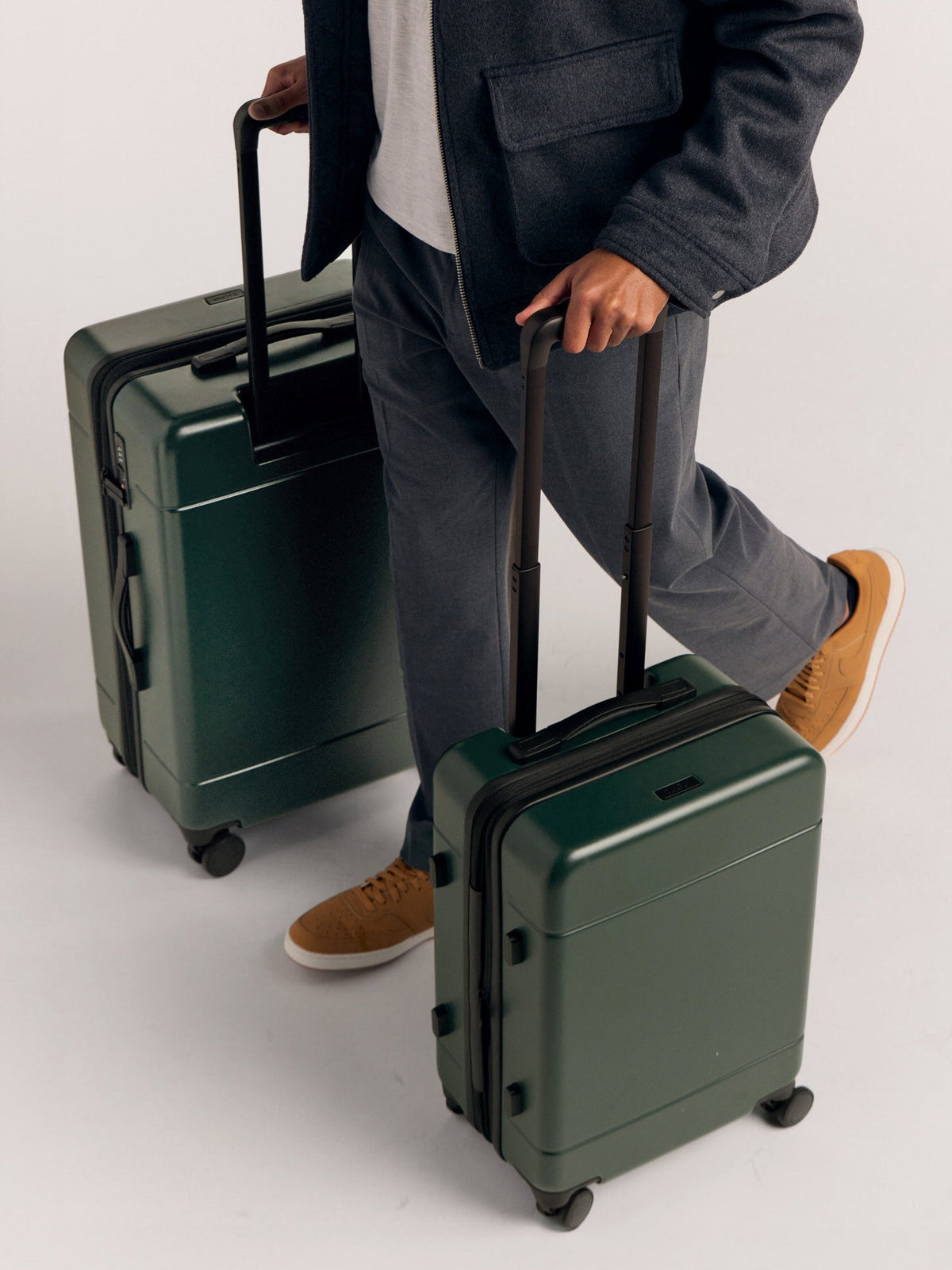 Model rolling the CALPAK Hue Medium & Large Luggage in green Emerald; LHU1024-EMERALD