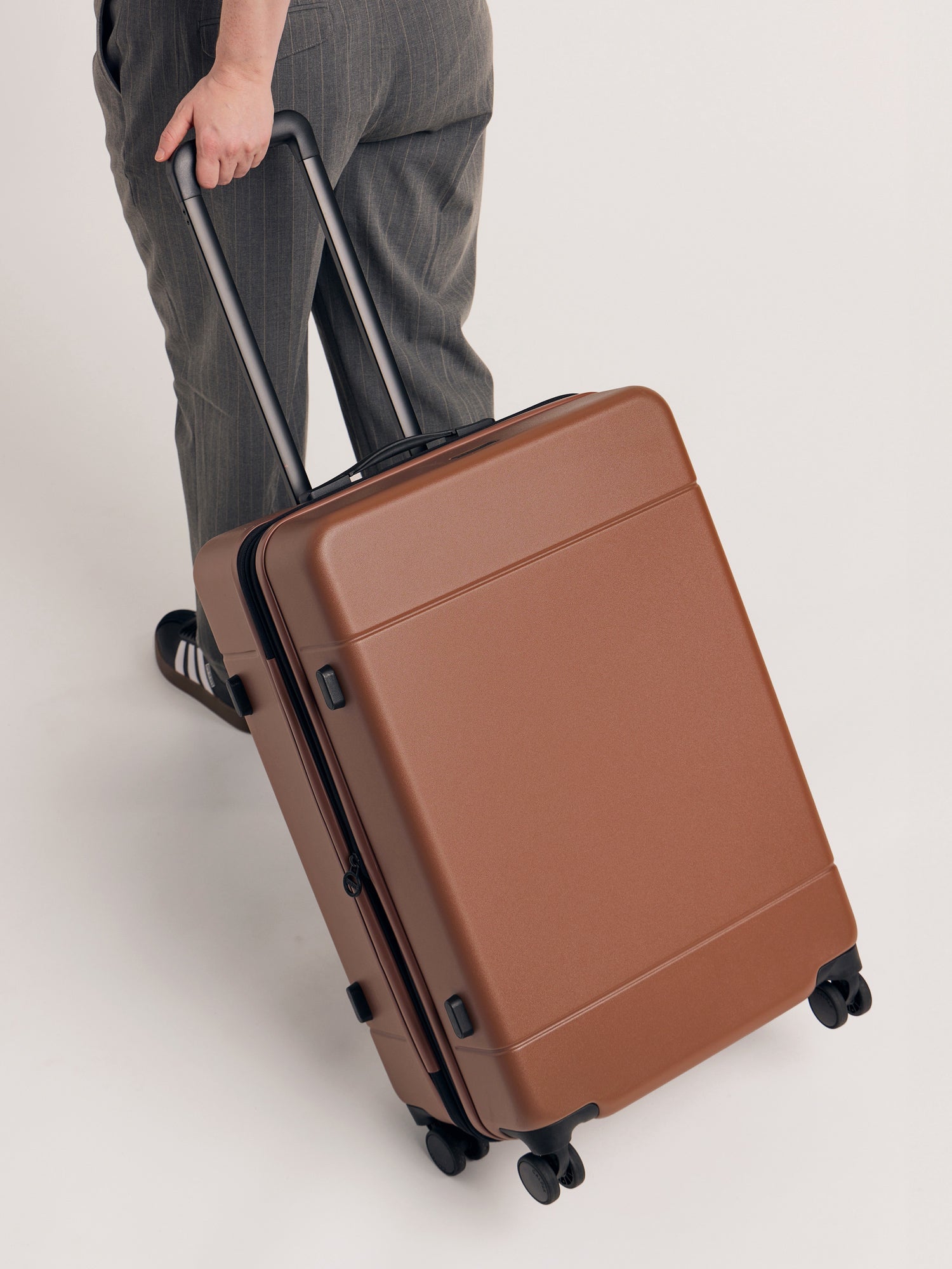 Model rolling with CALPAK Hue Medium Hardside Luggage in brown hazelnut; LHU1024-HAZEL 