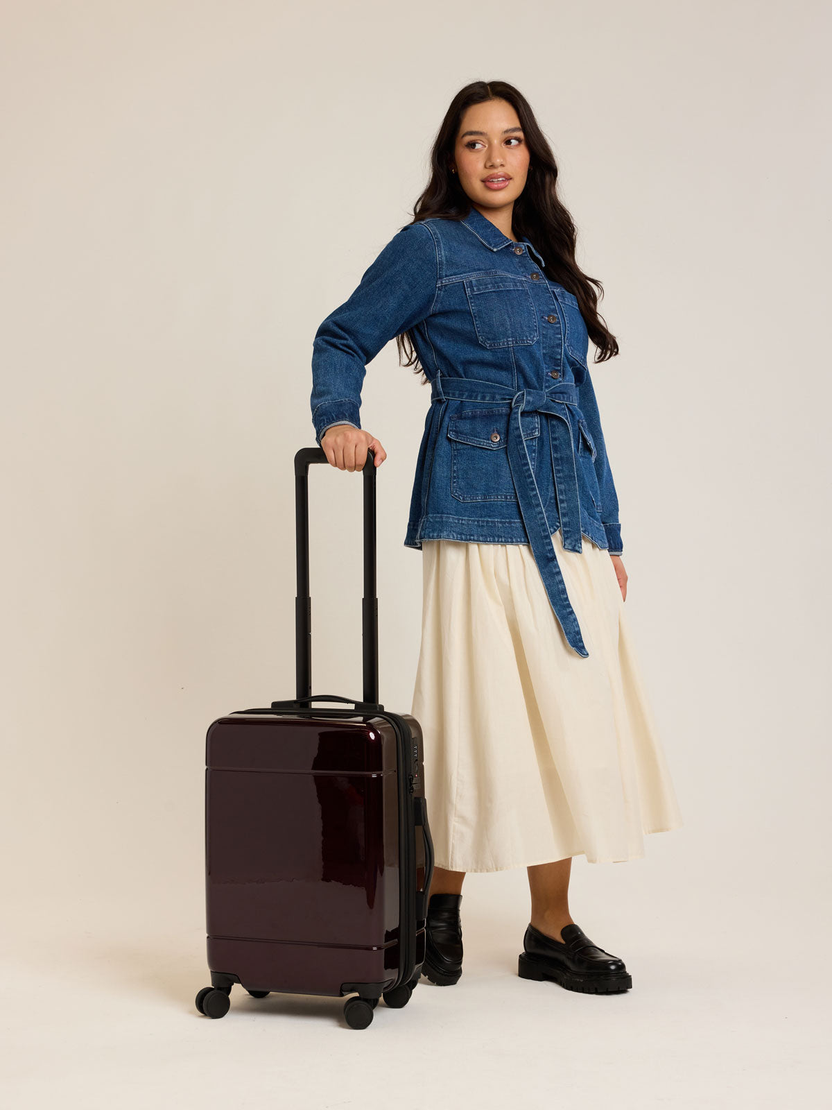 Model with CALPAK Hue Carry On Luggage in Dark Cherry Red on white background; LHU1020-NP-GLAZED-DARK-CHERRY