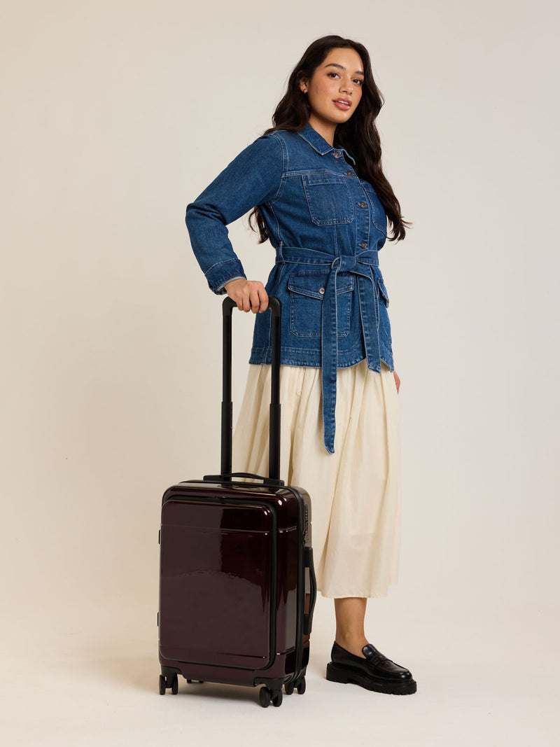 Model holding CALPAK Hue Front Pocket Carry On Luggage in maroon Glazed Dark Cherry