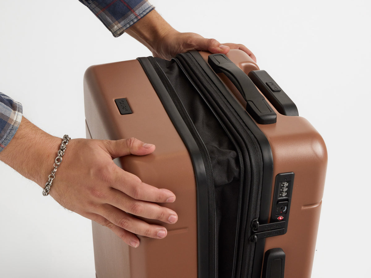 Model showing expansion ability of CALPAK Hue Carry-On luggage in brown