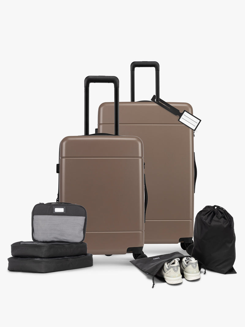 CALPAK Hue Starter Bundle in brown Chocolate that comes with Large and Carry On Luggage, Luggage Tag, Two Black Pouches, and Three Black Packing Cubes shown on a white background