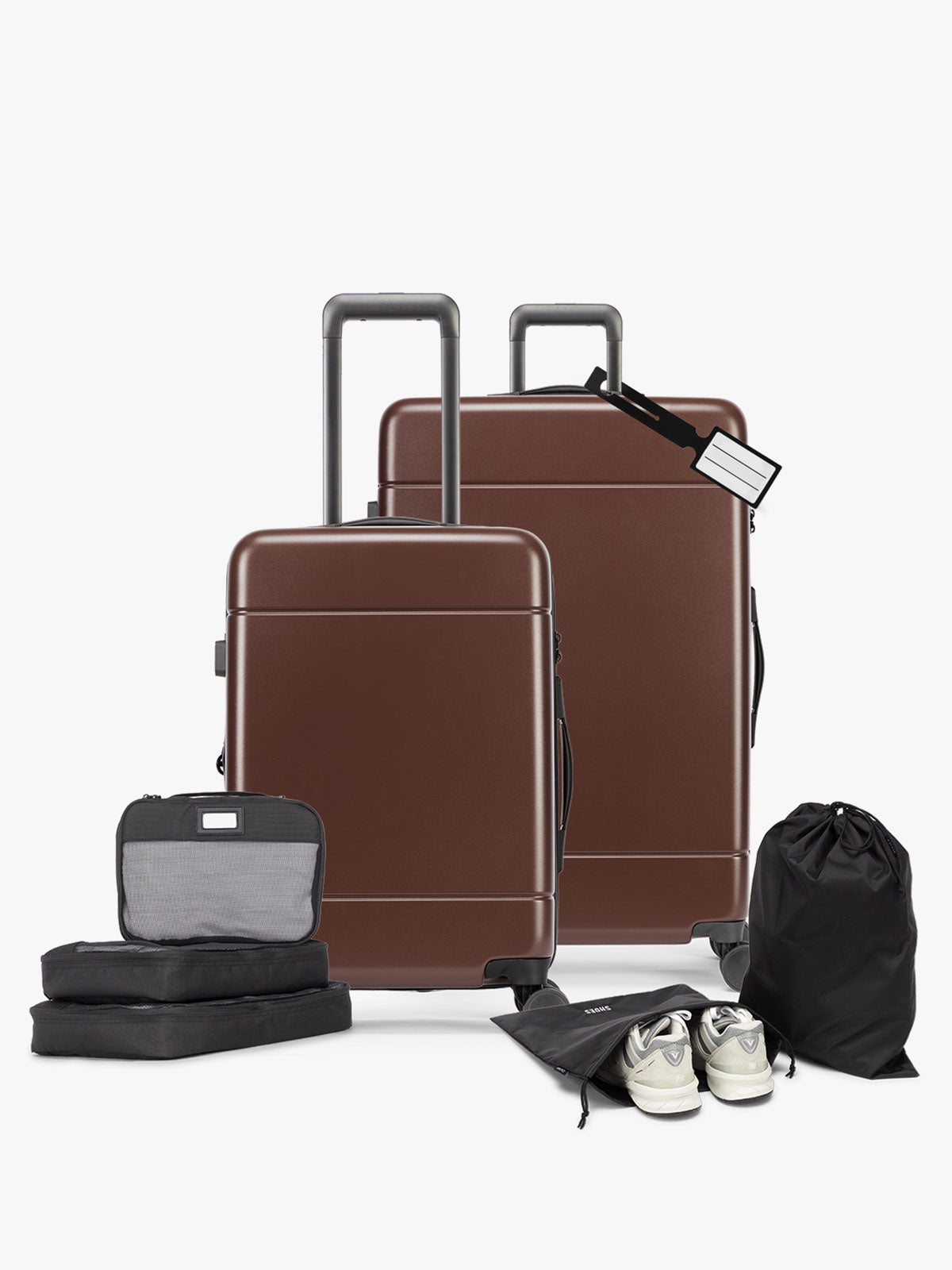 A 7-piece travel luggage set including two brown hard-shell suitcases, three black packing cubes, a black drawstring bag, a black shoe bag, and a pair of white sneakers, arranged on a clean white background featuring the CALPAK Hue Starter Bundle in brown Walnut; LHU8000-WALNUT