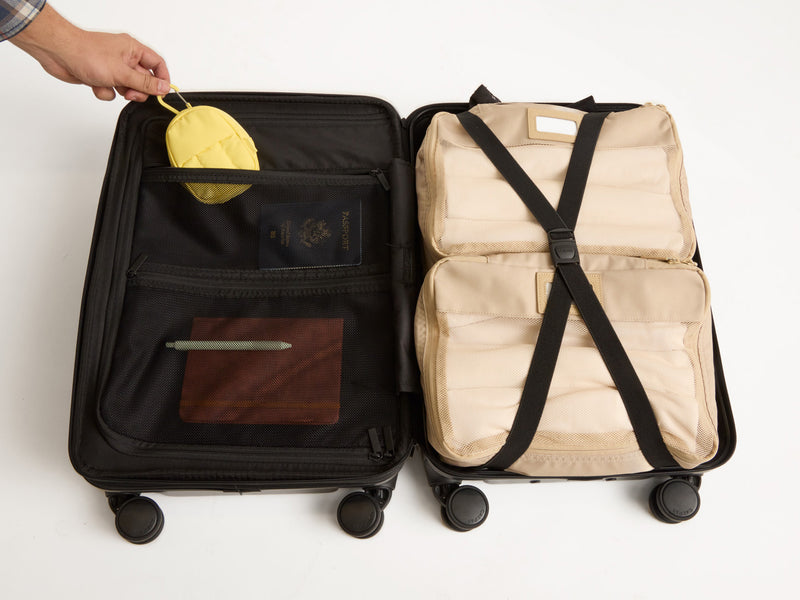 Interior shot of Hue Carry-On Luggage in black. Luggage is packed with two packing cubes, key pouch, passport and notebook