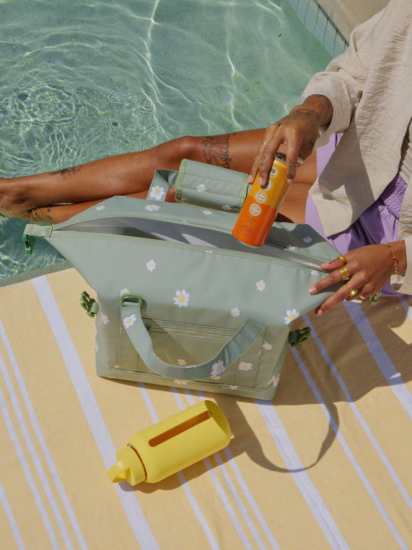 Model placing canned beverage into 17L insulated cooler bag with expandable sides for extra packing space in daisy print