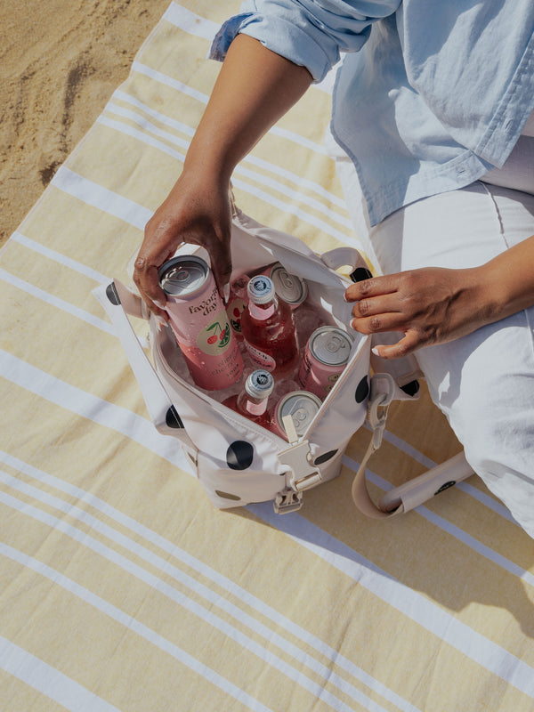 Model placing beverage on ice within CALPAK Insulated 8L Soft-Sided Cooler in polka dot at beach