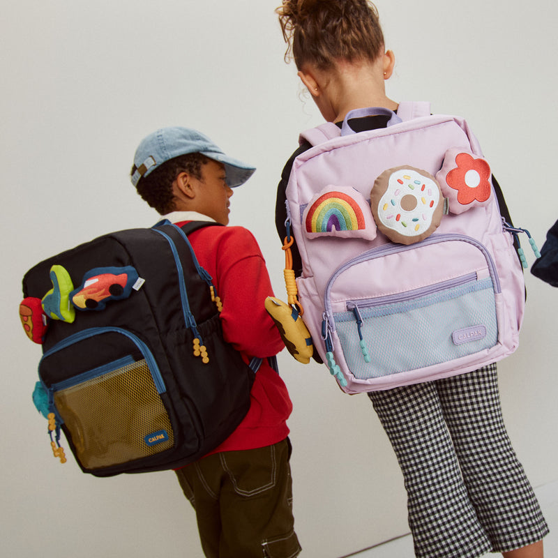 Two children with CALPAK Kids Collection backpacks featuring colorful decorations on a plain background