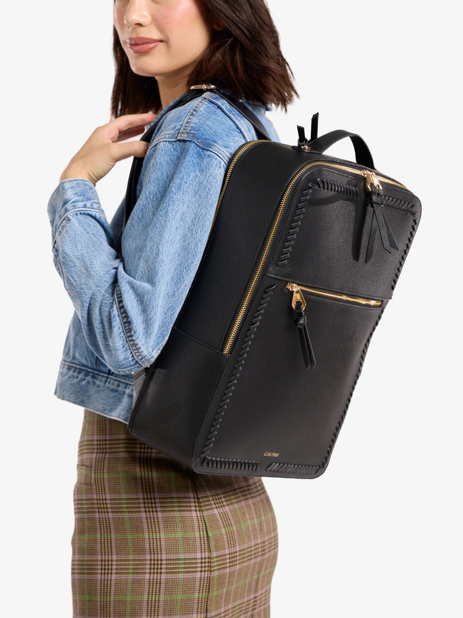 Model wearing CALPAK Kaya 17 inch Laptop Backpack in black with gold accents