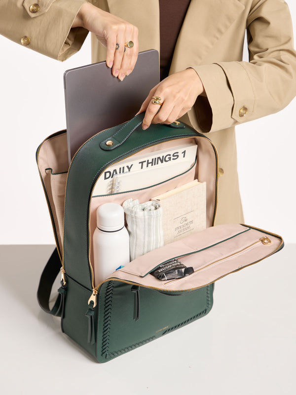 Model placing 17 inch laptop within laptop compartment of CALPAK laptop backpack in emerald green