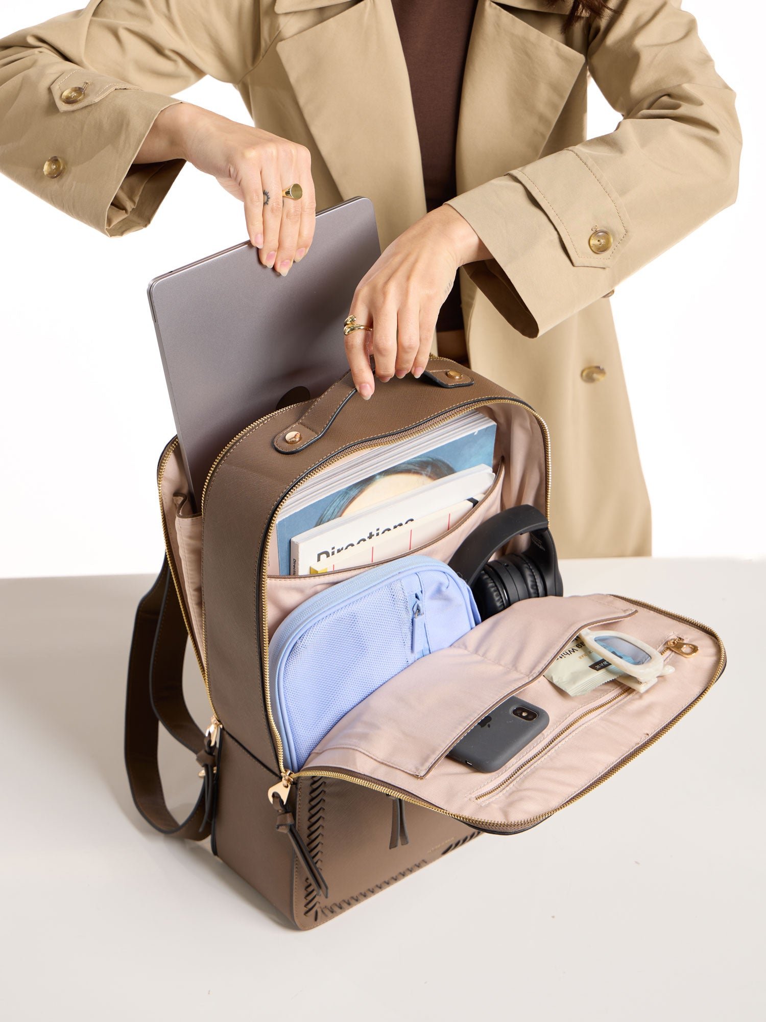 Model placing 17 inch laptop within laptop compartment of CALPAK laptop backpack in brown mocha
