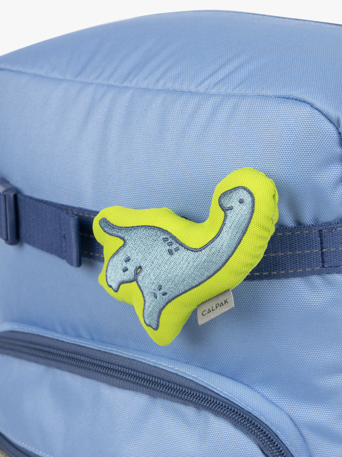 CALPAK Kids Collection blue and green Dinosaur Pluffy Bag Charm attached to Kids Large Blue Backpack; BCKM5000-BLUE