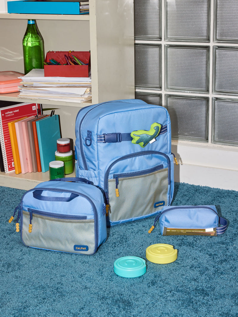 CALPAK Kids Collection Large Kids Backpack Bundle in Blue that includes Kids Lunch Bag, Kids Pencil Case, Rainbow Pluffy Bag Charm, and Set of 2 Ice Packs in a kid's room