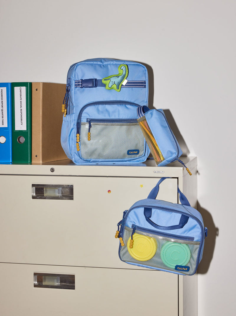 CALPAK Kids Collection Medium Kids Backpack Bundle in Blue that includes Kids Lunch Bag, Kids Pencil Case, blue and green Dinosaur Pluffy Bag Charm, and Set of 2 Ice Packs in a kid's room