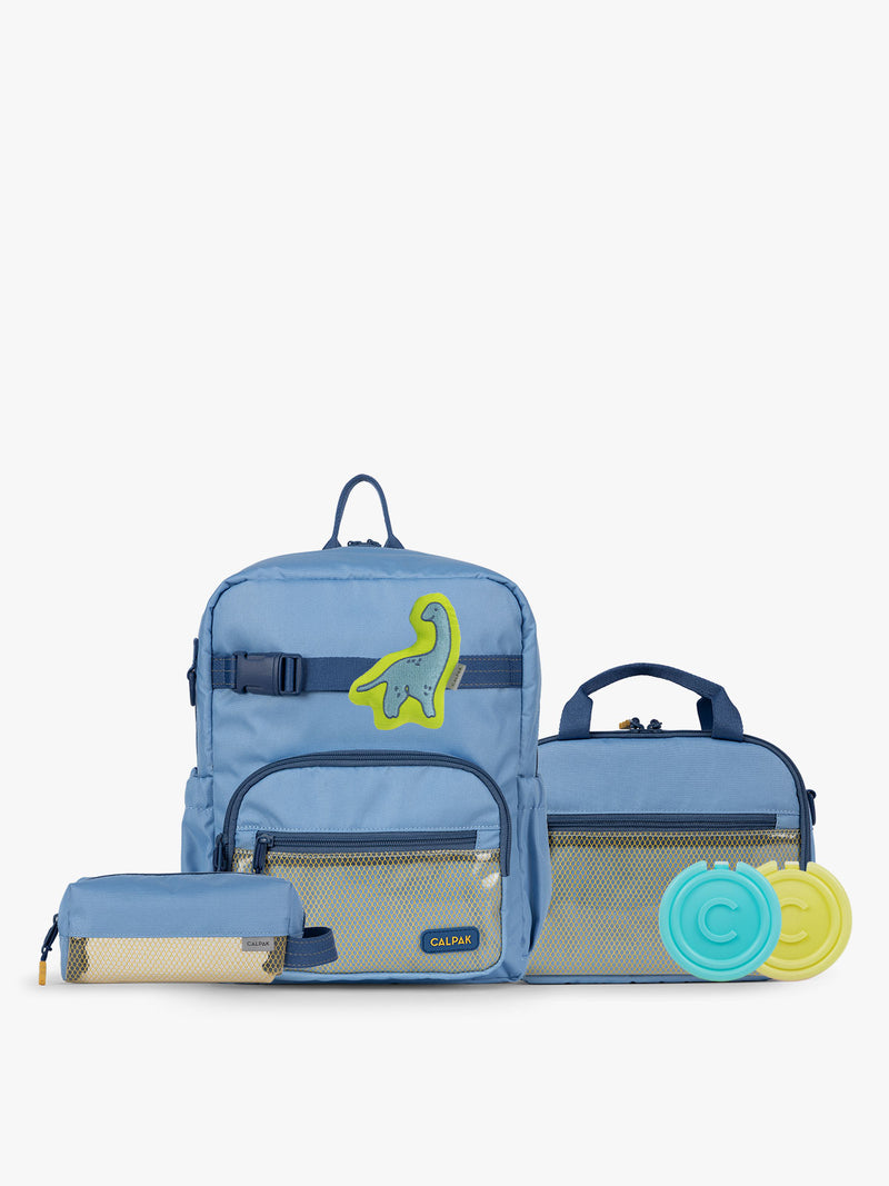 CALPAK Kids Collection Small Kids Backpack Bundle in Blue that includes Kids Lunch Bag, Kids Pencil Case, blue and green Dinosaur Pluffy Bag Charm, and Set of 2 Ice Packs in a kid's room
