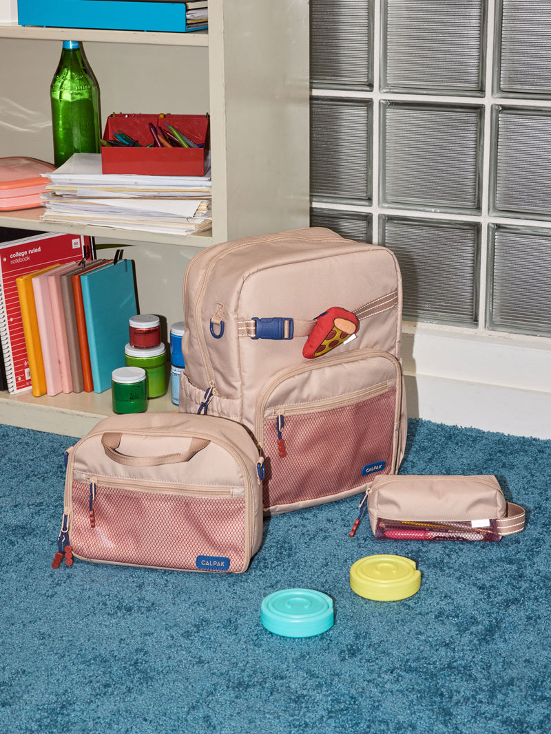 CALPAK Kids Collection Large Kids Backpack Bundle in brown/tan Khaki that includes Kids Lunch Bag, Kids Pencil Case, red and yellow PIzza Pluffy Bag Charm, and Set of 2 Ice Packs in a kid's room