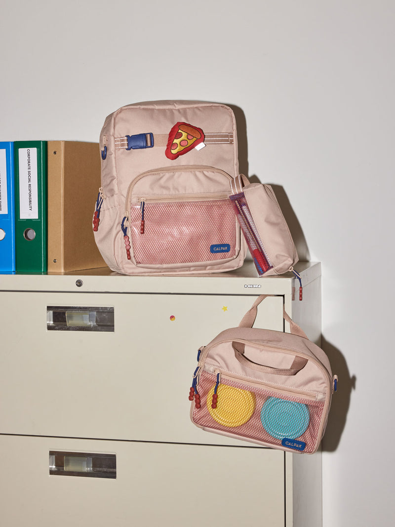 CALPAK Kids Collection Medium Kids Backpack Bundle in brown/tan Khaki that includes Kids Lunch Bag, Kids Pencil Case, red and yellow PIzza Pluffy Bag Charm, and Set of 2 Ice Packs in a kid's room