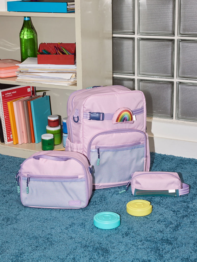 CALPAK Kids Collection Large Kids Backpack Bundle in pink lavender Orchid Pink that includes Kids Lunch Bag, Kids Pencil Case, Rainbow Pluffy Bag Charm, and Set of 2 Ice Packs in a kid's room